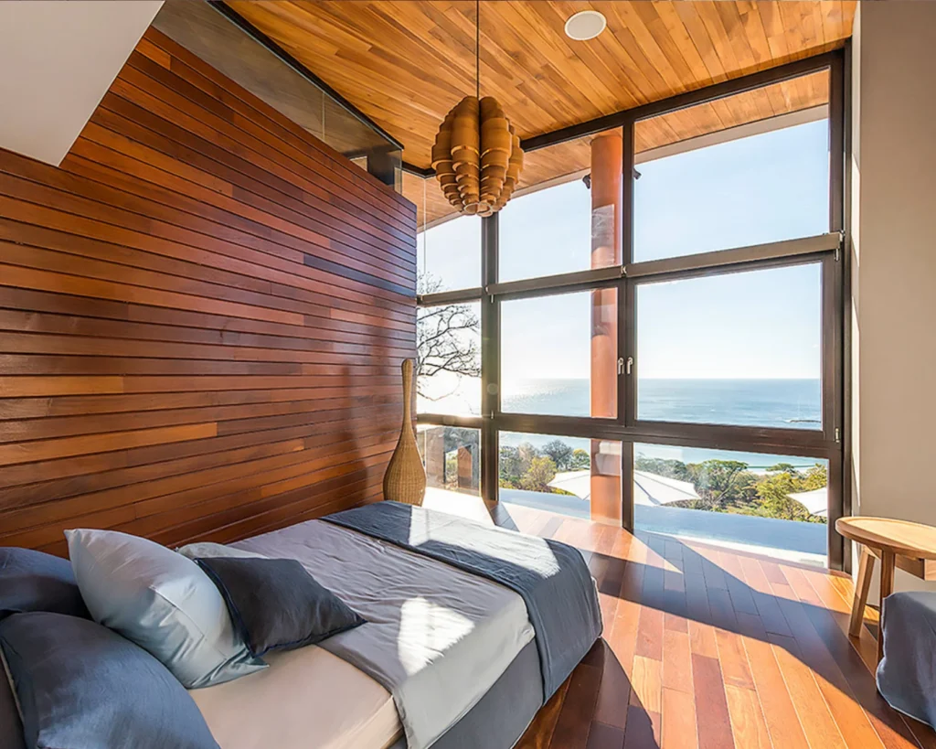 Habitación invitados con revestimiento en madera de teca y ventanales con vista al océano.