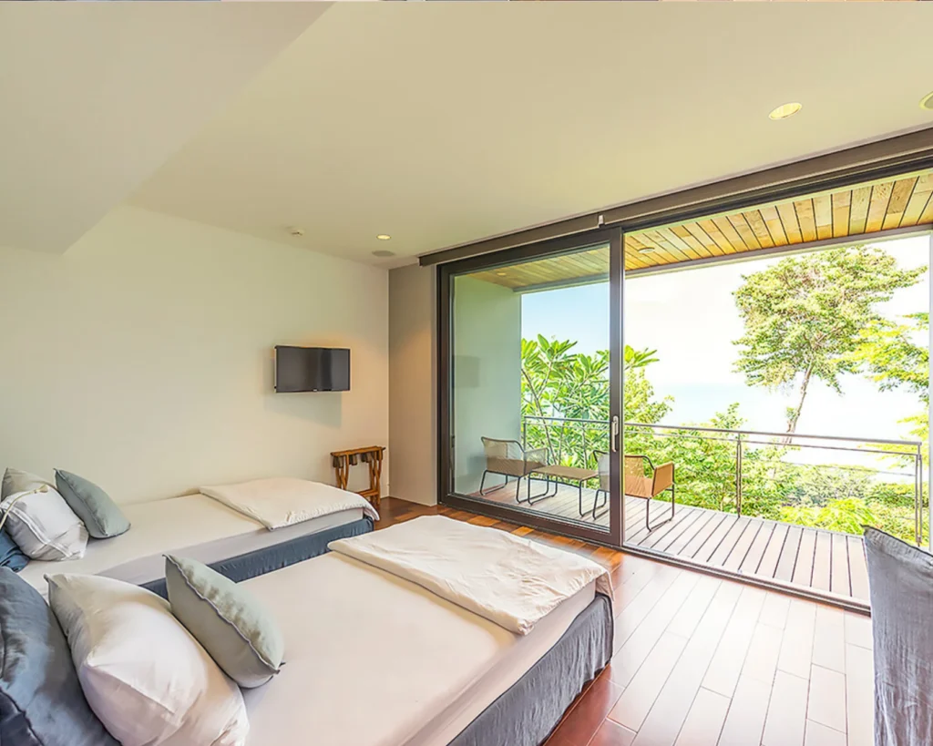 Habitación secundaria con balcón privado, piso de madera y vista al bosque tropical y mar.