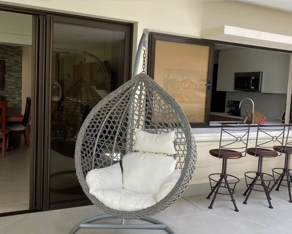 Zona de bar con sillas altas y silla colgante tipo cápsula en terraza moderna conectada al área interior de la casa