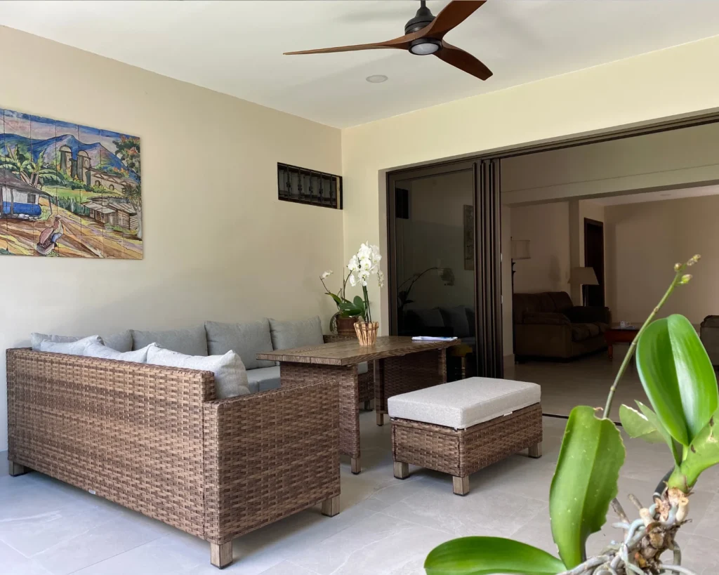 Área de estar con sofá de ratán, mesa auxiliar y decoración con orquídeas en terraza techada de estilo contemporáneo