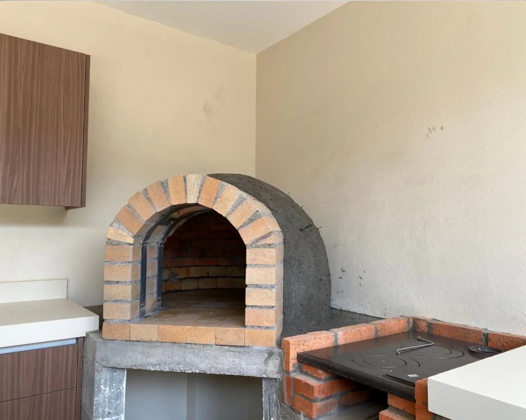 Detalle del horno artesanal de ladrillo refractario empotrado en mueble de concreto junto a cocina de leña