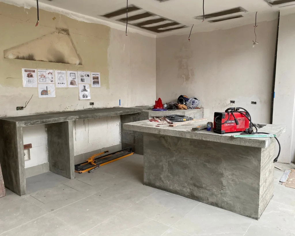 Proceso de construcción de muebles en concreto para cocina exterior y bar en terraza techada, con estructura en obra gris y planos en la pared