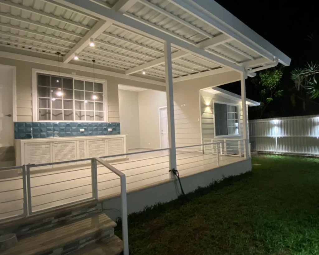Vista general de terraza y jardín iluminado, con bar de apoyo y lámparas colgantes.