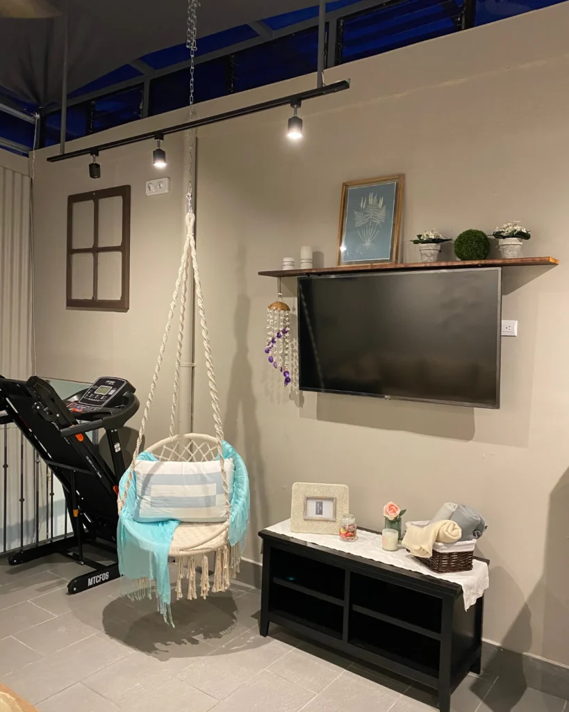 Vista nocturna con riel de luces encendido, silla colgante, televisor y consola; se observa caminadora al fondo.